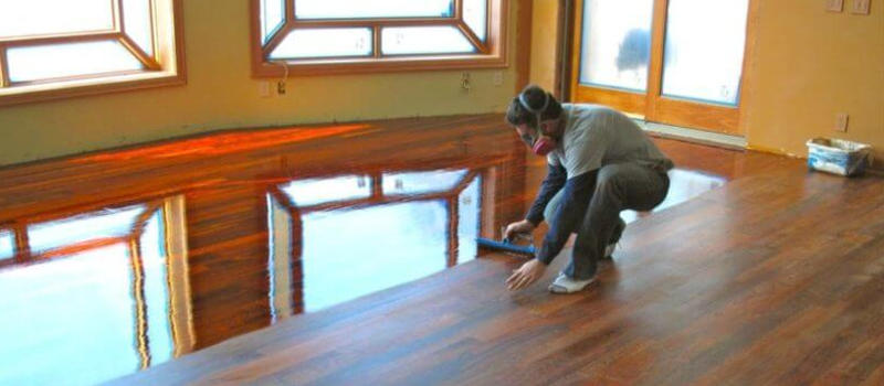 contractor applying polyurethane to wood floor