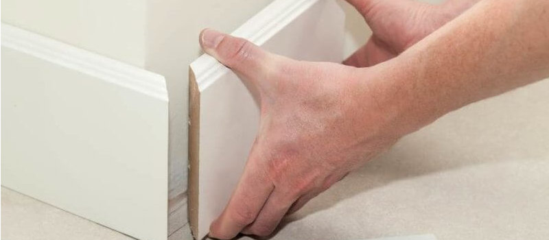close up of hands removing baseboard away from wall